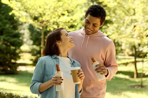 Una coppia elegante e diversificata che si gode reciprocamente compagnia mentre tiene tazze di caffè in un ambiente vivace parco. — Foto stock
