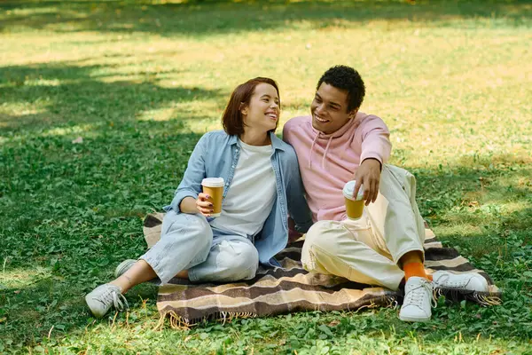 Ein Mann und eine Frau in lebendiger Kleidung sitzen auf einer Decke im Gras und genießen Gesellschaft in einer friedlichen Parklandschaft. — Stockfoto