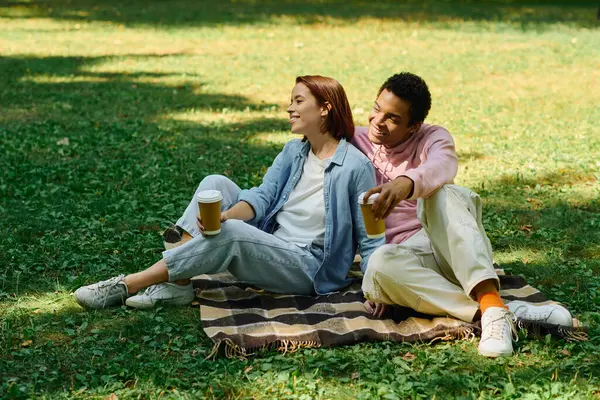 A diverse couple in vibrant attires sitting on a blanket in the grass, enjoying each others company. — Photo de stock