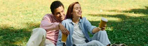 Un couple aimant et diversifié en tenue vibrante assis sur l'herbe, profitant d'un moment paisible dans le parc. — Photo de stock