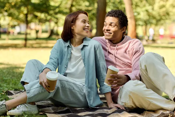 A diverse couple in vibrant attires sitting on a blanket, enjoying a peaceful moment together in a park. — Photo de stock