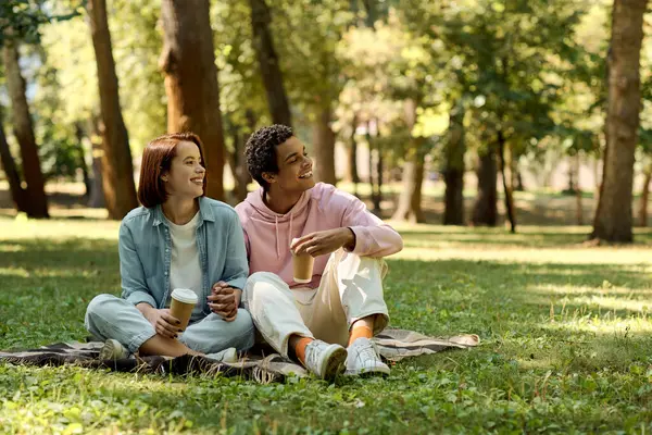 Una pareja diversa en traje vibrante disfrutando de un momento tranquilo sentado en una manta en un parque. - foto de stock
