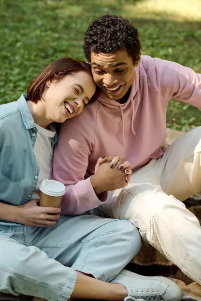 Un couple diversifié en tenue vibrante s'assoit paisiblement sur le terrain, profitant mutuellement de la compagnie dans un cadre de parc. — Photo de stock
