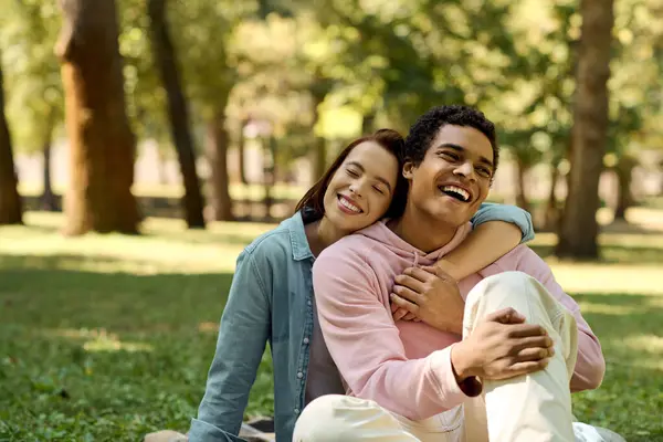 Un hombre y una mujer están sentados en la hierba en un parque, vestidos con trajes vibrantes, abrazándose en un momento de serenidad. - foto de stock