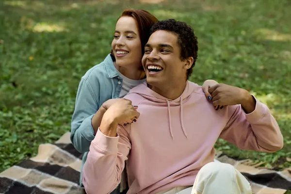Un homme et une femme en tenue vibrante assis sur une couverture ensemble dans un parc, profitant d'un moment paisible ensemble. — Photo de stock