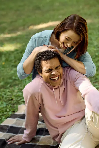 A loving couple, dressed in vibrant attire, relax in a park as the man sits on top of the woman on a colorful blanket. — Stock Photo