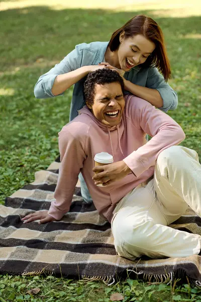 Un couple aimant et diversifié assis sur une couverture colorée dans un parc, partageant des moments intimes ensemble. — Photo de stock