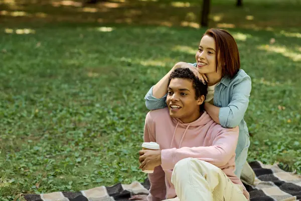Una coppia, vestita in modo vivace, seduta su una coperta in un parco, che condivide un momento di intimità in mezzo a un verde lussureggiante. — Foto stock