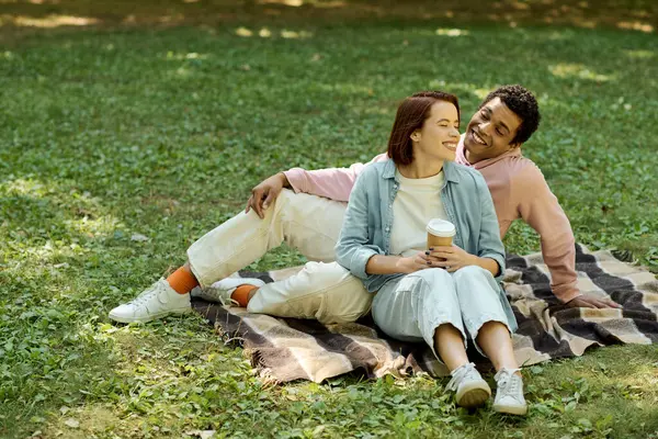Un homme et une femme en tenue vibrante s'assoient sur une couverture dans l'herbe, profitant d'un moment paisible ensemble dans le parc. — Photo de stock