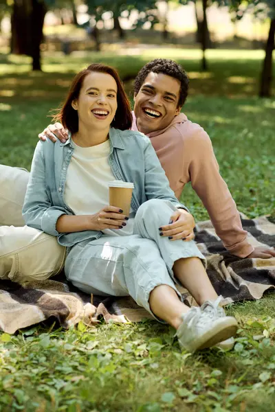 Diversa pareja en traje vibrante sentados juntos en una manta, disfrutando de un momento tranquilo en el parque. - foto de stock