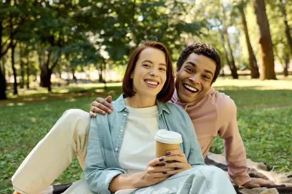 A diverse couple in vibrant attire relaxes on a blanket in a park, enjoying a peaceful and intimate moment together. — Stock Photo