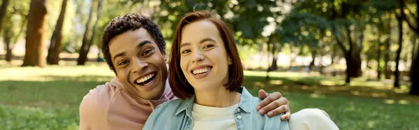 A diverse, loving couple in vibrant attire enjoying a relaxing moment together in a grassy park. — Stock Photo