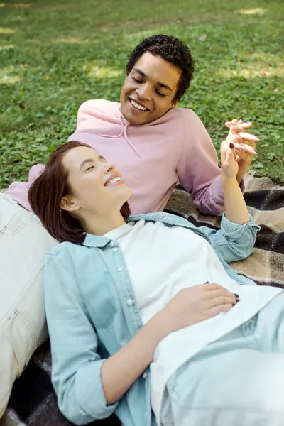 Un uomo e una donna in abiti vivaci giacevano insieme su una coperta nell'erba, godendo di un momento di relax nel parco.. — Foto stock