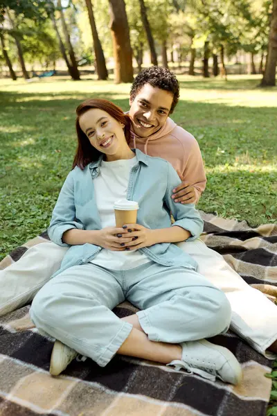 Um casal amoroso diversificado em trajes vibrantes se senta em um cobertor, compartilhando um momento terno no parque.. — Fotografia de Stock