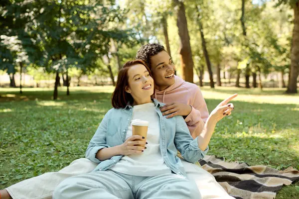 Живая, разнообразная пара в красочной одежде сидит на одеяле в парке, наслаждаясь спокойным моментом вместе. — стоковое фото