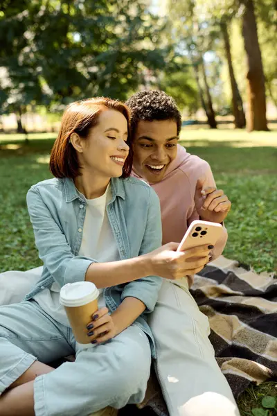 Різноманітна пара, одягнена яскраво, сидить на ковдрі в парку, насолоджуючись компанією один одного в мирній обстановці. — стокове фото