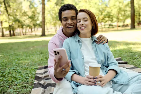 Un hombre y una mujer vestidos con estilo se sientan en una manta, sonriendo y disfrutando de la compañía de los demás en un entorno vibrante parque. - foto de stock