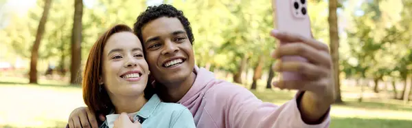 A diverse loving couple, dressed vibrantly, capturing a happy moment together as they take a selfie in a park. — Stock Photo