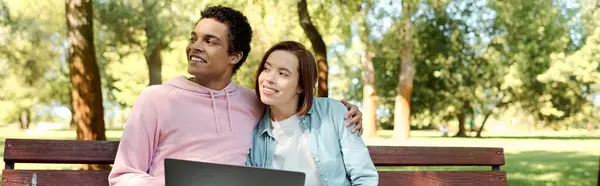 Un uomo e una donna in abiti vibranti si siedono su una panchina del parco, assorti in un computer portatile, godendo di un appuntamento digitale. — Foto stock