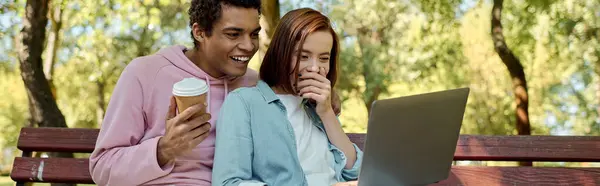 Diverse couple in vibrant attire sitting on park bench, engrossed in laptop screen. — Stock Photo