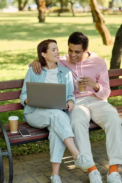 Ein vielseitiges Paar in lebendiger Kleidung sitzt auf einer Bank, vertieft in einen Laptop-Bildschirm inmitten der ruhigen Parklandschaft. — Stockfoto
