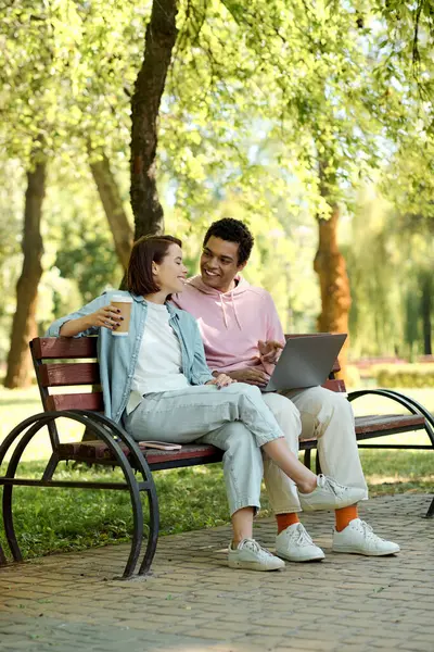 Un couple élégamment habillé, immergé dans le monde numérique, assis sur un banc de parc, absorbé par l'écran d'un ordinateur portable. — Photo de stock