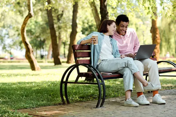 A couple in vibrant attires sit on a bench, engrossed in their laptop. — Stock Photo
