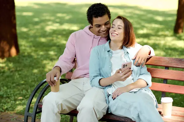 Un couple diversifié en tenue vibrante assis sur un banc de parc, profitant de l'autre compagnie par une journée ensoleillée. — Photo de stock