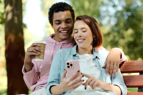 Una pareja diversa en traje vibrante se sienta en un banco, absorto en un teléfono celular juntos. - foto de stock