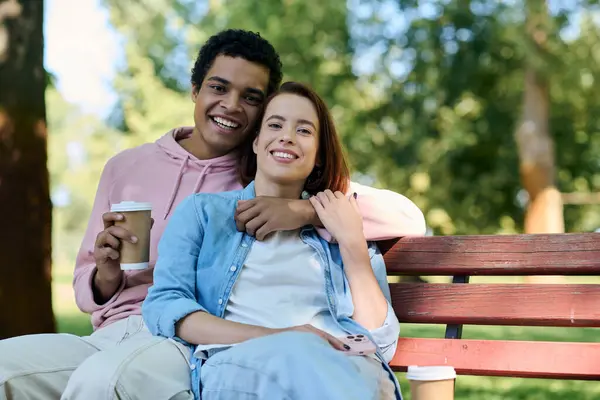 A diverse couple in vibrant attire sits together on a park bench, enjoying each others company in a serene setting. — Stock Photo