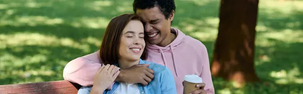 Un couple diversifié en tenue vibrante partageant une étreinte aimante sur un banc de parc. — Photo de stock
