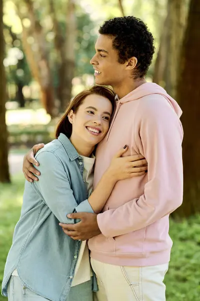 Чоловік у яскравому одязі ніжно обіймає жінку в парку, демонструючи момент близькості та зв'язку в природній обстановці. — стокове фото
