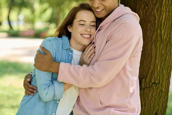 Чоловік і жінка в яскравому одязі ніжно обіймаються перед величним деревом в парку, демонструючи їх глибокий зв'язок. — стокове фото