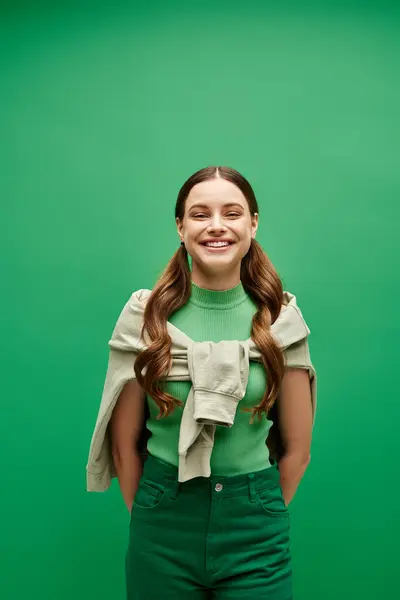 A young woman in her 20s stands elegantly in front of a vibrant green background in a studio setting. — Stock Photo