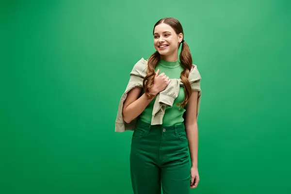 A stunning young woman in her twenties standing gracefully against a vibrant green backdrop in a studio. — Stock Photo