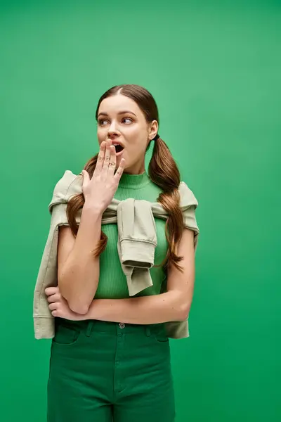 Uma jovem mulher bonita na casa dos 20 em pé na frente de um fundo verde vibrante, exalando surpresa — Fotografia de Stock