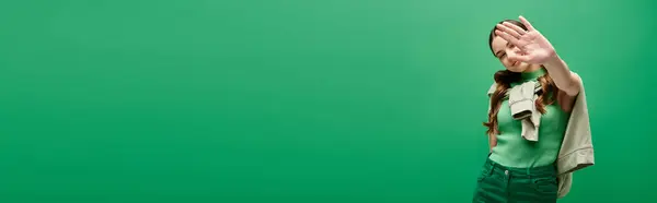 A young woman in her 20s stands gracefully in front of a vivid green backdrop, exuding a sense of mystery and allure. — Stock Photo