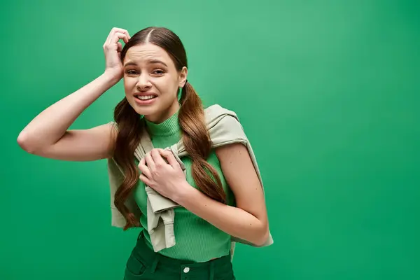 Confused woman in her 20s with long hair, standing gracefully in front of a vivid green background. — Stock Photo