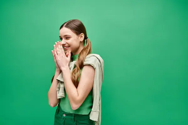 Una giovane donna felice sulla ventina si trova fiduciosa di fronte a un vivido sfondo verde in un ambiente da studio. — Foto stock