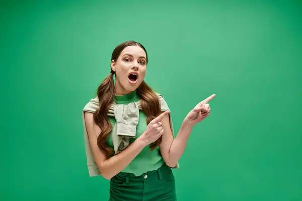 Eine junge Frau in ihren Zwanzigern, in einem grünen Hemd, zeigt mit neugieriger Miene auf etwas aus dem Off.. — Stockfoto