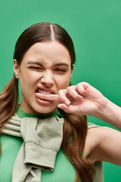 Daring young woman in her 20s playfully making a face in a studio setting on a green backdrop. — Stock Photo