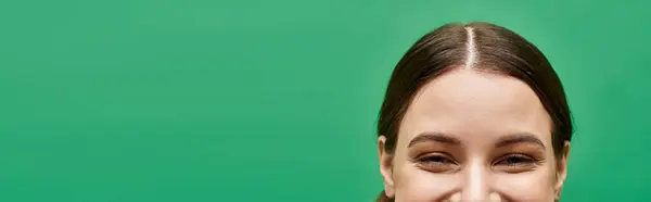 A young woman in her 20s smiles warmly against a vibrant green background in a studio setting. — Stock Photo