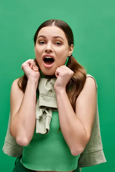 A young woman in her 20s looks shocked and surprised in a studio setting against a green backdrop. — Stock Photo