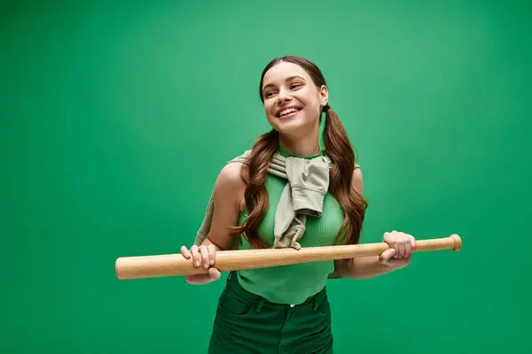 A woman in her 20s holds a baseball bat against a vibrant green backdrop, exuding strength and determination. — Stock Photo