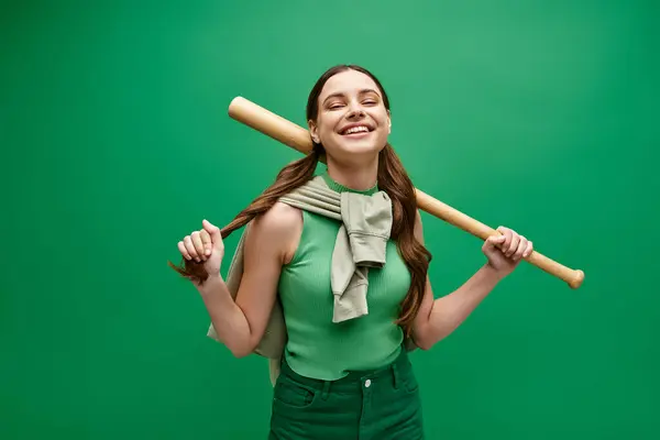 A young woman in her 20s confidently holds a baseball bat in a studio setting against a vibrant green background. — Stock Photo