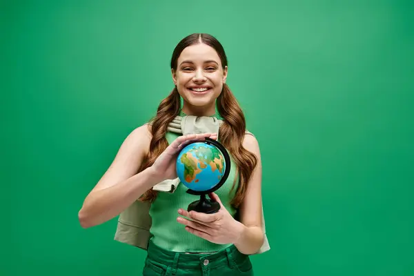 Junge Frau in ihren Zwanzigern mit einer kleinen Weltkugel in der Hand vor ateliergrünem Hintergrund. — Stockfoto