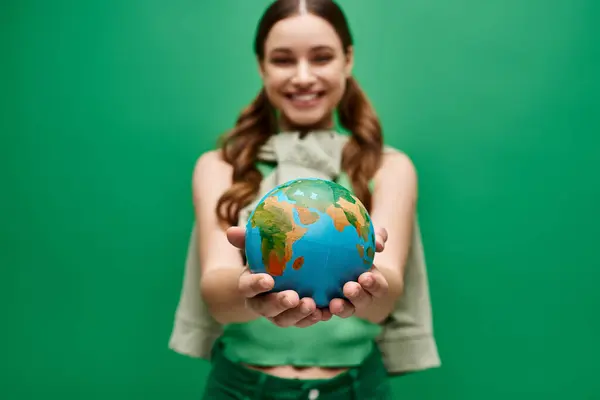 A young woman in her 20s gently holding a small globe in her hands in a studio setting on green background. — Stock Photo