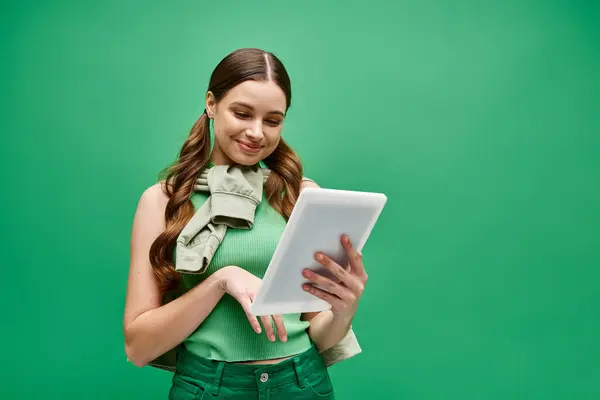 Une femme élégante dans la vingtaine, portant une chemise verte, tient avec confiance une tablette dans un cadre de studio. — Photo de stock