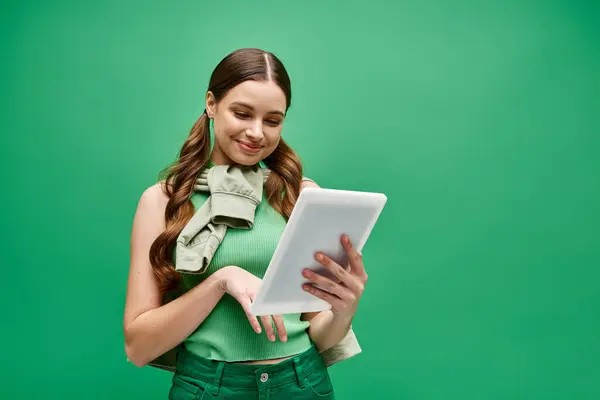 A stylish woman in her 20s, wearing a green shirt, confidently holds a tablet in a studio setting. — Stock Photo