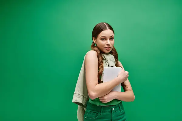 A stunning young woman in her 20s, clad in a green shirt, holds a tablet in a captivating studio setting. — Stock Photo